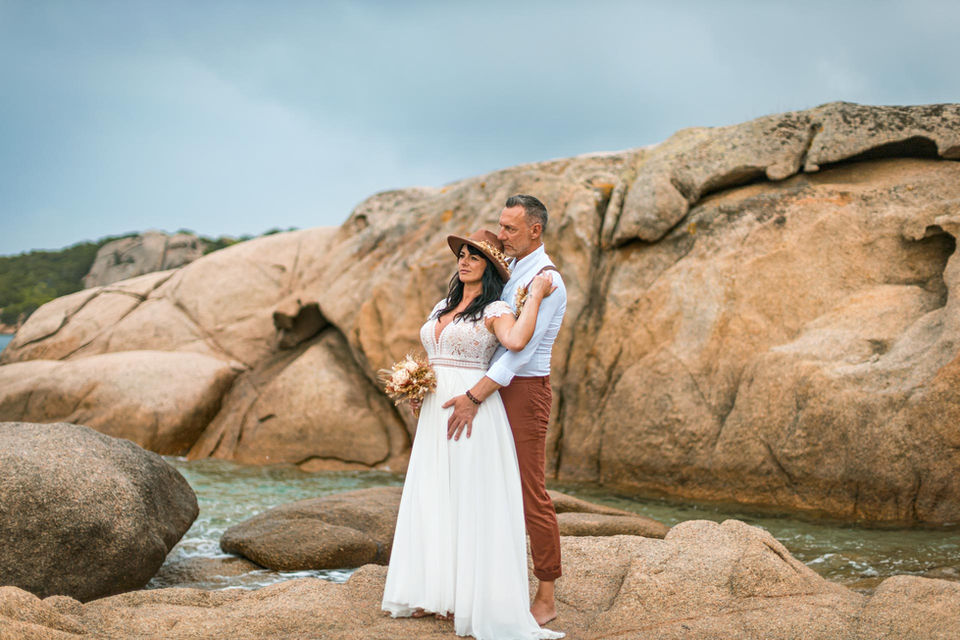 Am Strand von Sardinen steht ein Hochzeitspaar auf den Felsen