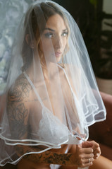 woman seated on dark mauve couch, wearing white lingerie and white bridal veil for bridal boudoir photoshoot in Phoenix, Arizona