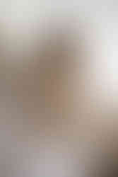 pregnant woman sitting on bed in white gown and talking on vintage phone for maternity boudoir