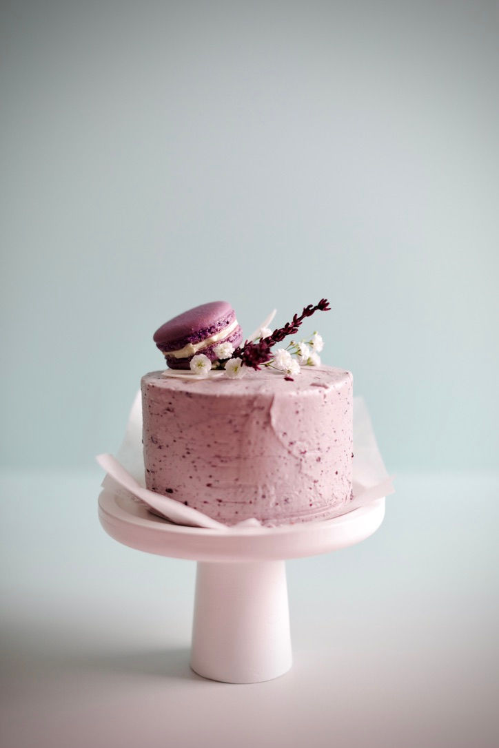 Pink bento cake on a pedestal, decorated with a purple macaron and chocolate accents.