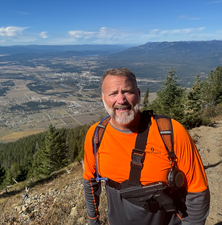 Smiling man in orange shirt hiking with valley overlook.