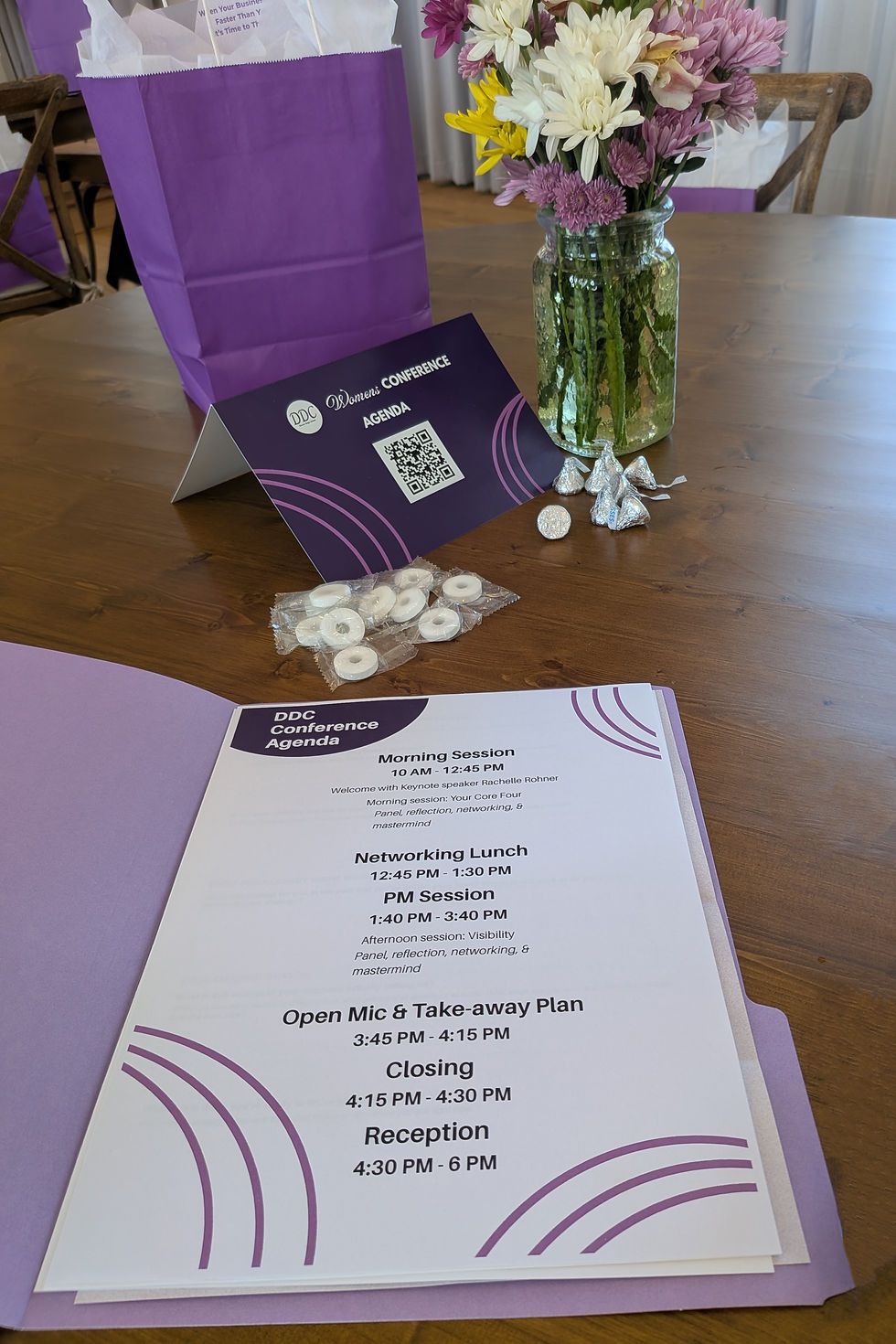 A photo of the agenda that we designed for the DDC Conference. This agenda was placed in a purple folder and is displayed next to table displays that we also designed that feature the same purple and circle theme.