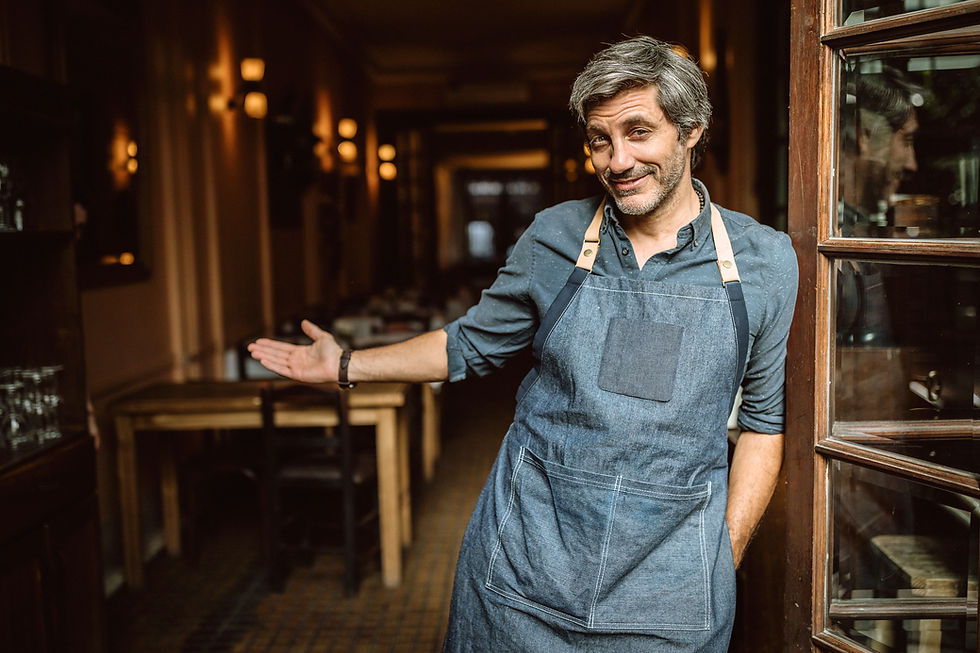 Un hombre con delantal en la puerta de un restaurante invitando a entrar