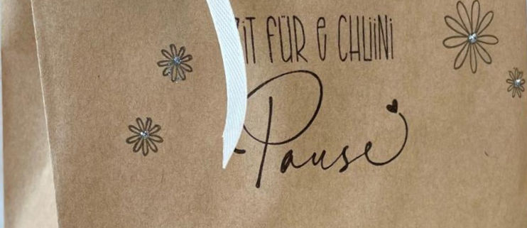 Ausschnitt einer Kraftpapiertüte mit dem Spruch, Zit für e chlini Pause. Verziert mit hübschen Blümchen