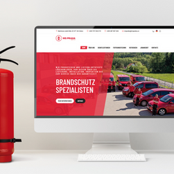 Ein Feuerlöscher steht links neben einem Computer auf die Webseite eines Brandschutz-Spezialisten aufgerufen ist.