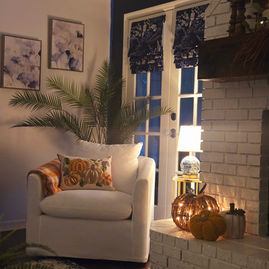 Cozy Tampa Bay living room corner with white armchair, pumpkin pillow, plaid blanket, and autumn decor by a brick fireplace.