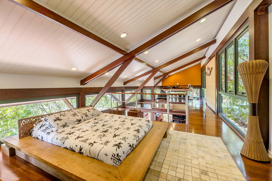 Dormitório aconchegante em mezanino com cama baixa estilo tatame, vigas de madeira aparentes e teto inclinado, feito pela RM Arquitetura