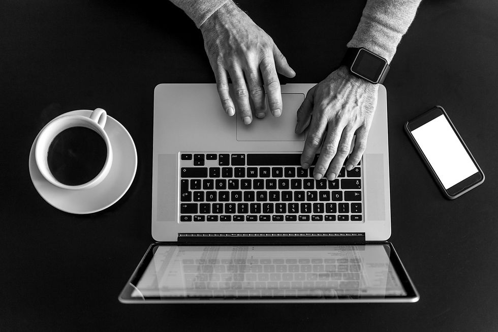 Profissional digitando no notebook com celular e xícara de café ao lado, em ambiente de trabalho de psicanálise.