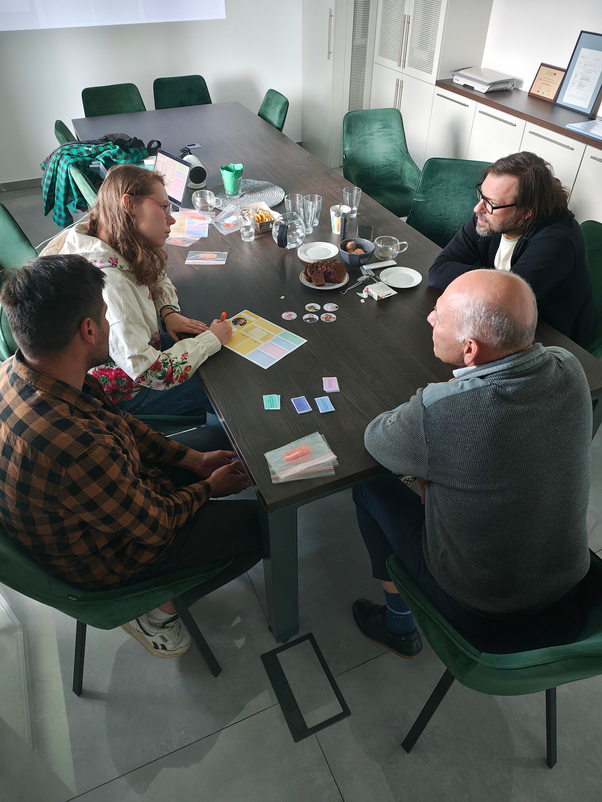 Workshop participants sit around a table and work in teams to develop a persona using printed persona cards and supplementary materials.