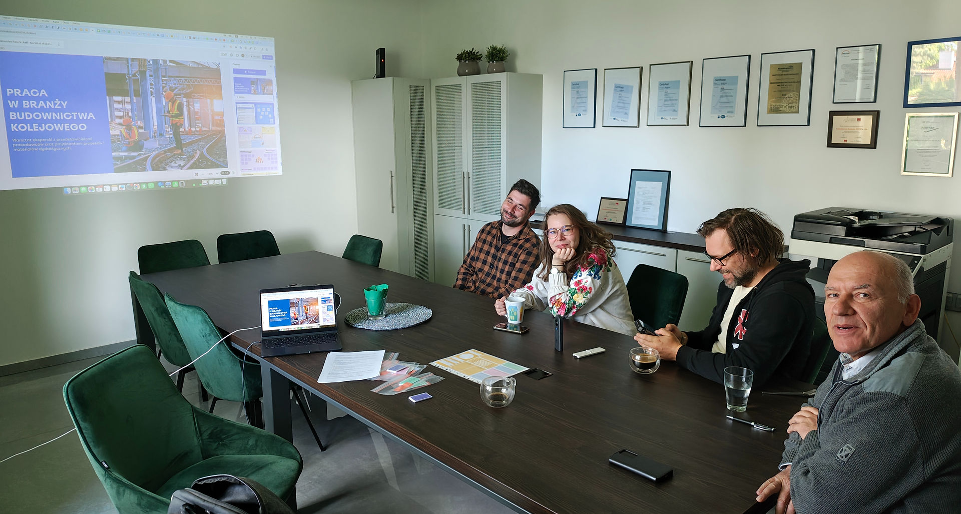 Participants in an expert workshop are seated at a conference table. A presentation slide is projected on the wall.