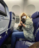 Mujer rubia con mascarilla, sosteniendo perro pequeño en asiento de avión.