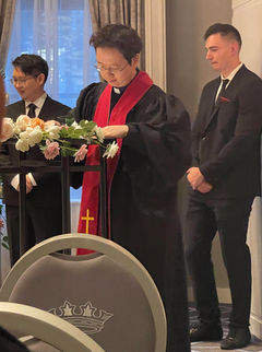 Pastor Paul signing marriage documents on a tall table with 2 groomsmen in the background.