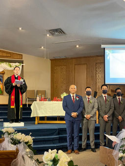 Wedding officiant Pastor Paul on the stage with the groom & groomsmen standing together on side.