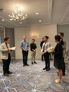 Small venue wedding rehearsal with Pastor Paul on the left, groom, bride, and bride's father on the right, and groomsmen in the back.