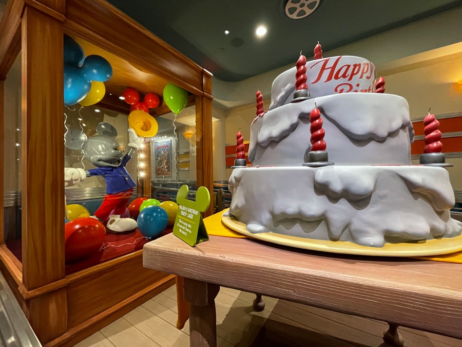 Mickey Mouse Birthday Party cake and costume props located inside the queue for Mickey and Minnie's Runaway Railway at Disneyland Park located within Mickey's Toontown.