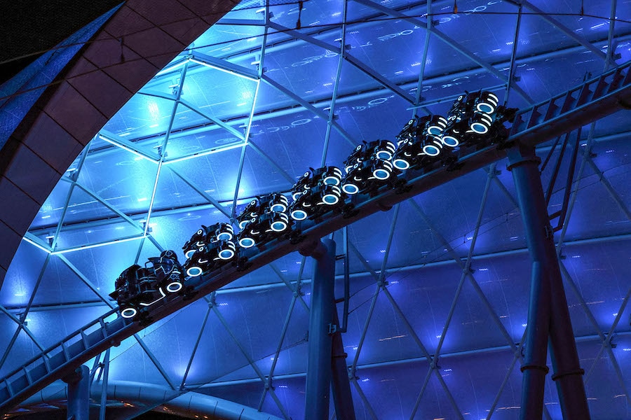 Lightcycle and Light Runner vehicles pass under a canopy in blue