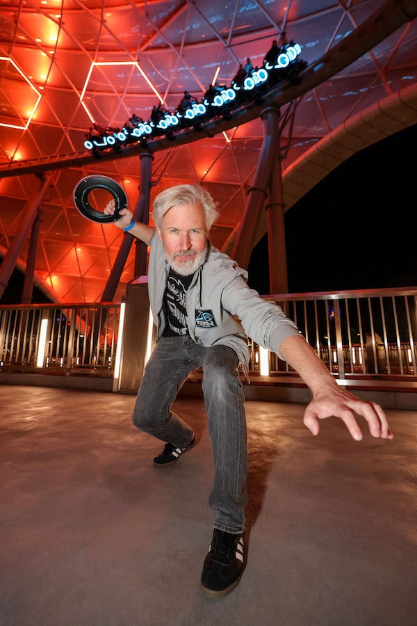 Steven Miller in front of Lightcycle and Light Runner vehicles passing under canopy