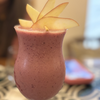 Blueberry smoothie in a tall glass, garnished with apples