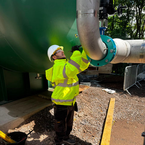 Worker in high-visibility jacket inspecting industrial pipes