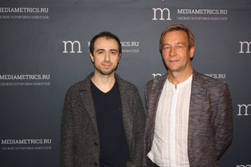 Loran Jacobs and Vladimir Konyshev standing together before an illuminated Mediametrics studio backdrop.