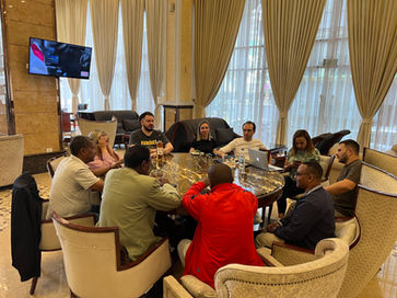 Loran Jacobs and a group of business professionals in suits sitting around a round table inside a bright office.