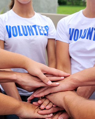 A group of people putting their hands together in a cirlce like a team would, wearing volunteer shirts