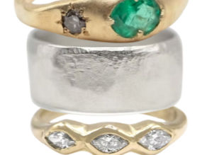 A gold and emerald ring, stacked with as silver and gold ring.