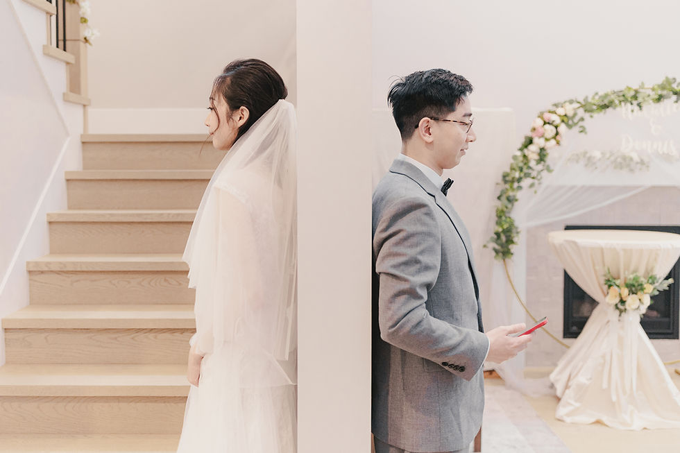 Bride in veil and groom in gray suit stand back-to-back by a pillar at a floral wedding venue, calm and formal