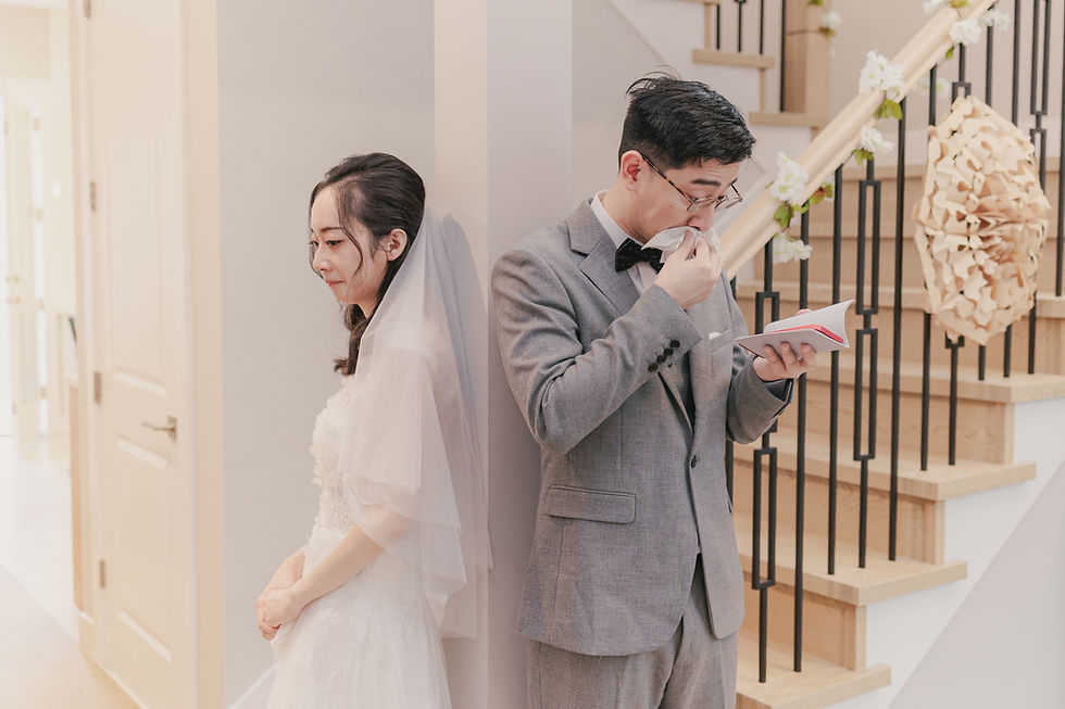 Bride and groom stand back-to-back at a stairway, both emotional; he reads a note, she in white veil looks down.