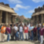 A group of approximately eighteen young travelers in colorful casual summer outfits posing together along the grand symmetric
