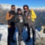 Three friends in layered winter trekking jackets, sunglasses, and a black beanie standing on a snow-covered Himalayan mountai