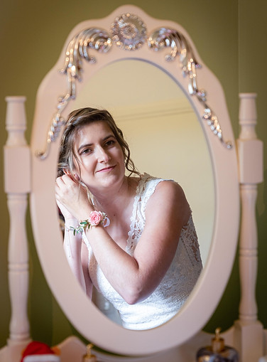 La mariée se prépare et met nses boucles d'oreilles en se regardat dans un miroir.