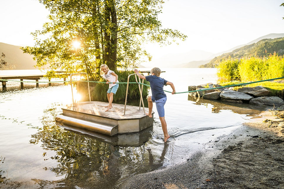 Kinder spielen am Seeufer, Seilziehen auf schwimmenden Steg