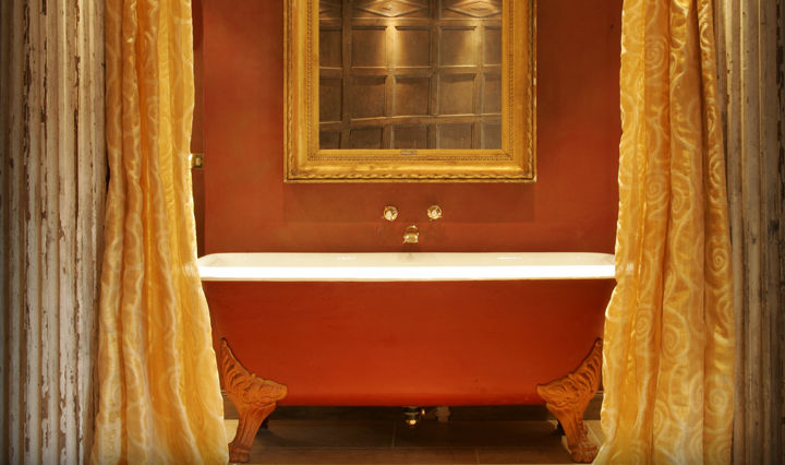 Traditional bath in a red hotel room with a gold mirror and golden gauze curtains with white text overlaid