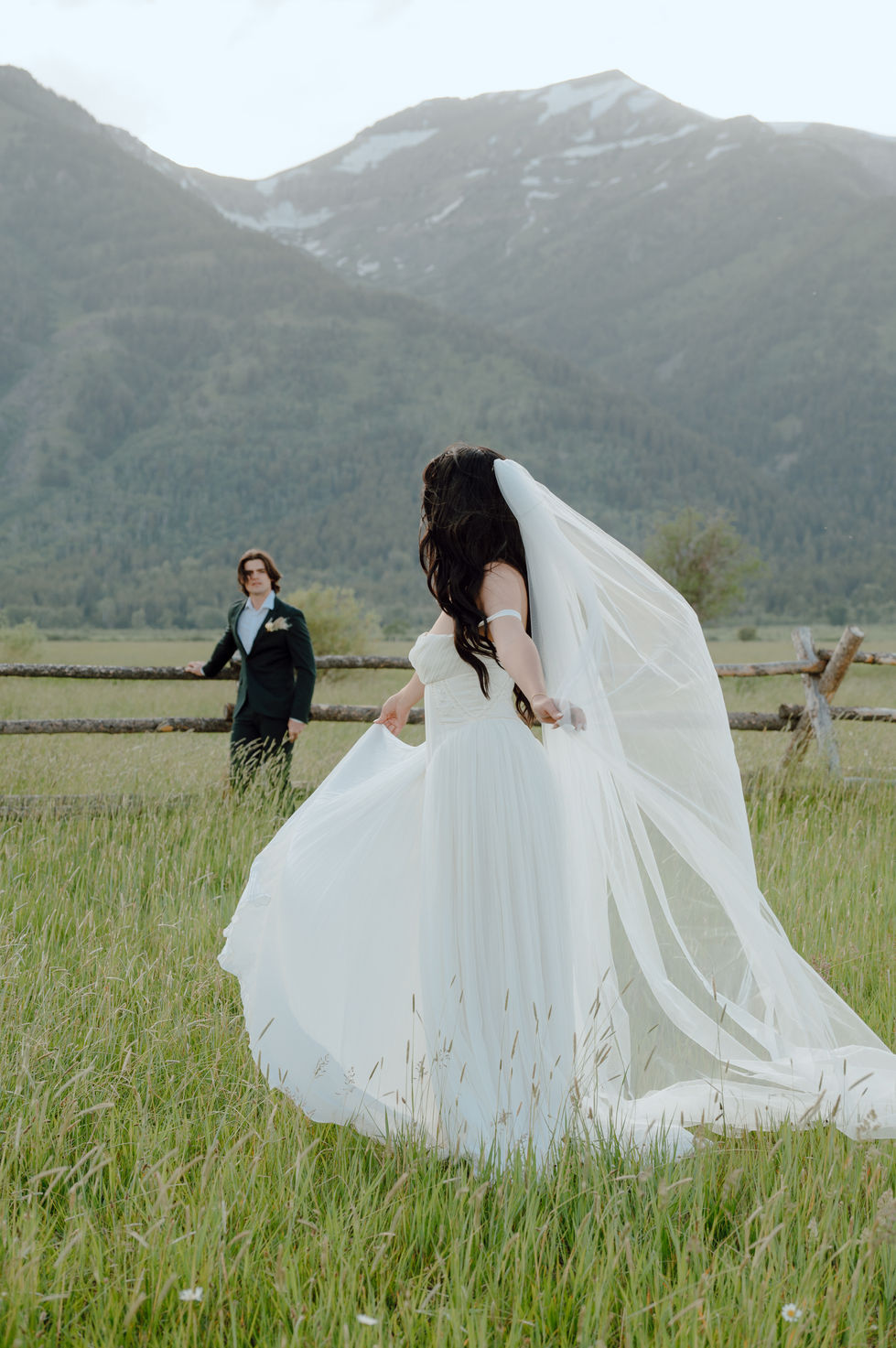 couple portraits next to Grand Tetons Mountains with Bride looking back at her groom with dress and veil flying in wind