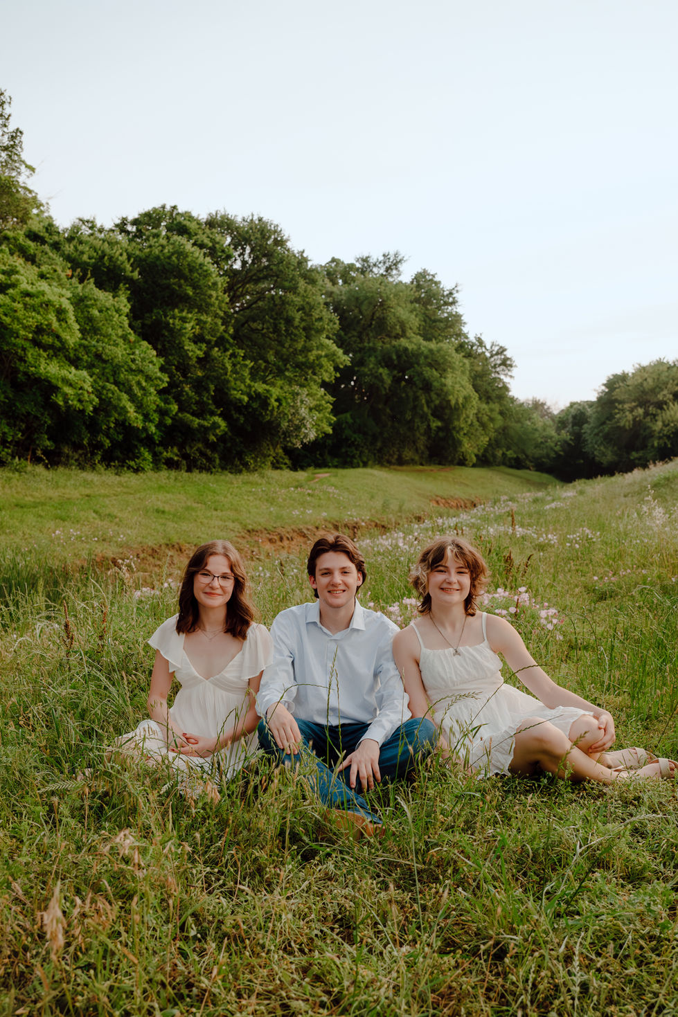 Senior triplet siblings laying in grass in wildflowers during senior pictures in Keller near Dallas Fort Worth