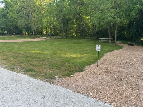 Individual campsites at a campground with marker signs, fire pits, and picnic tables 