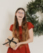 Braunhaarige Frau hält ein Weihnachtspäckchen und lacht in die Kamera.