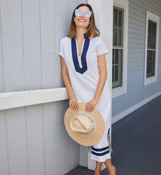 Gabriela Dias wearing white and navy tunic dress holding a straw hat in Rye, New York.
