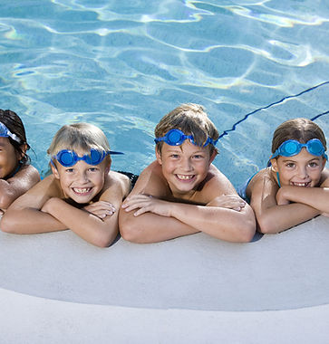 A photo of four kids learning on their elbows on the side of a pool