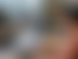 Woman in pink shirt works on laptop displaying charts and AI chatbot thread in bright, modern NZ office. Colleagues talk or are focused on their screens. Large windows, plants.