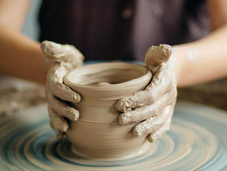 Clay-covered hands shaping a pottery bowl on a wheel during a mindful pottery session.