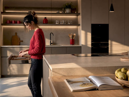 Una mujer ordena su cocina moderna y llena de luz, colocando cada cosa en su sitio para que todo quede perfecto.