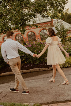 Couple holding hands walking outside a building with flowers and Engagement Photography Shaun and Zoe.