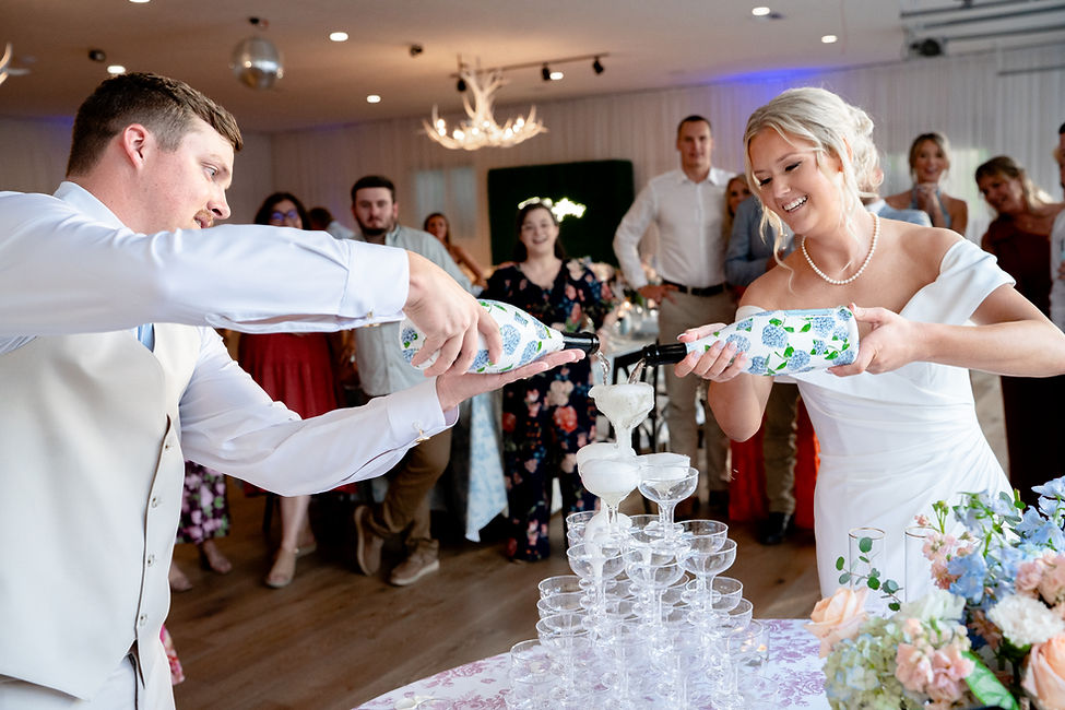 Bride and groom pour champagne into tower of glasses at wedding reception.