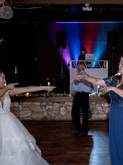 Bride and mother dancing at wedding reception with DJ in background.