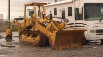 A yellow bulldozer is parked next to a white RV, creating a contrast between the vibrant and neutral colors.