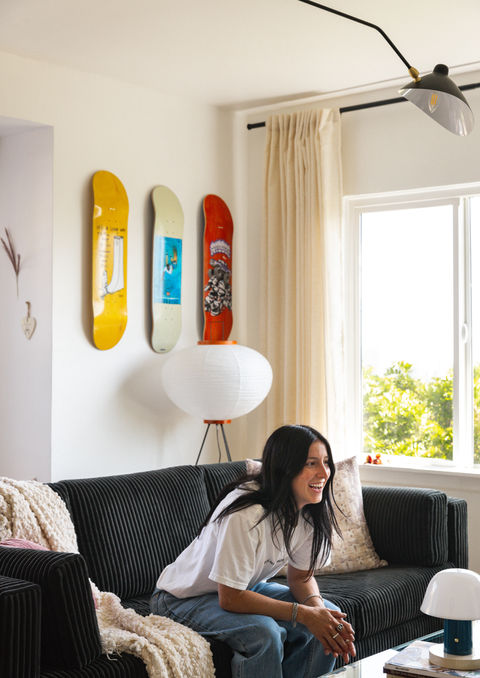 Person (Nicole hause) sitting on a black sofa in a bright living room decorated with colorful skateboard decks and a paper floor lamp in Hause House.