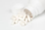 A white pill bottle with no label tipped on its side spilling white pills onto a white surface.