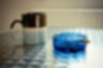 An ash tray containing a lit cigarette and a coffee mug sitting next to each other on a table.